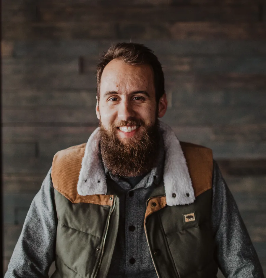 Luke Burgett smiling indoors in a corduroy and sherpa-collar jacket, with a wood-paneled wall in the background