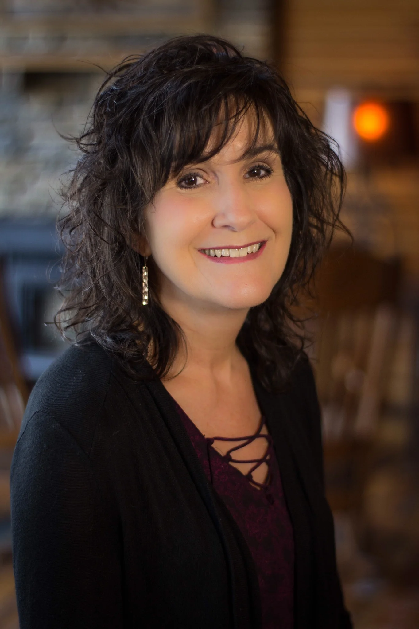 Rhonda Gore smiling indoors in a black cardigan, with a stone fireplace in the background